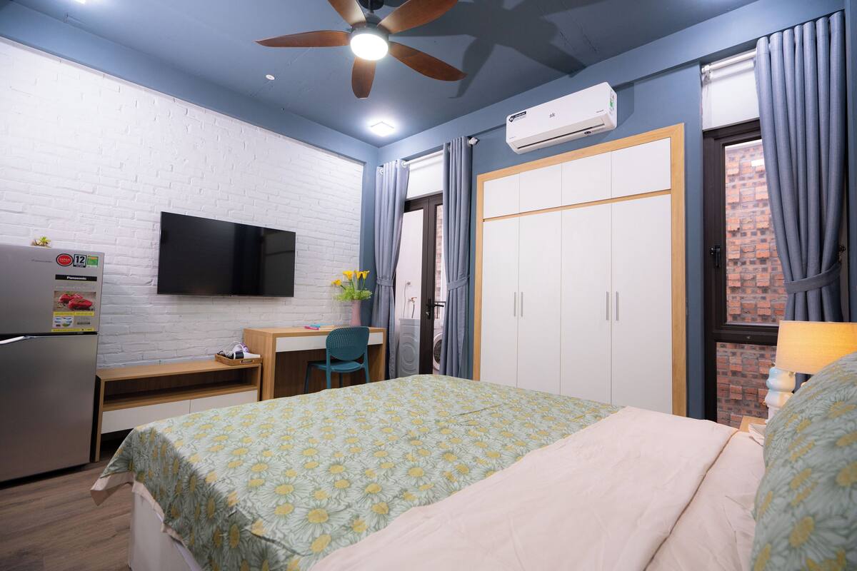 A bedroom with a bed, a desk, a chair, a television, and an air conditioning unit.