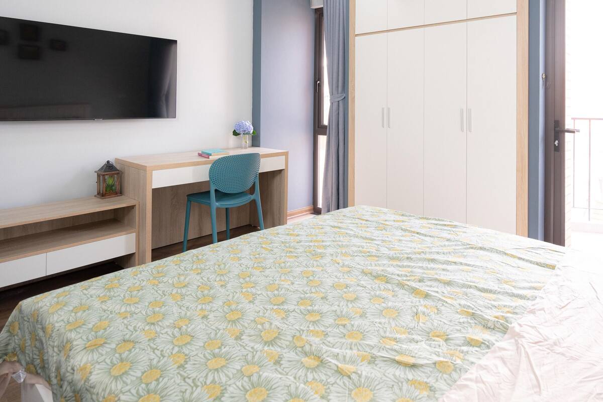 A bedroom with a bed, a desk, a chair, a TV, and a wardrobe.