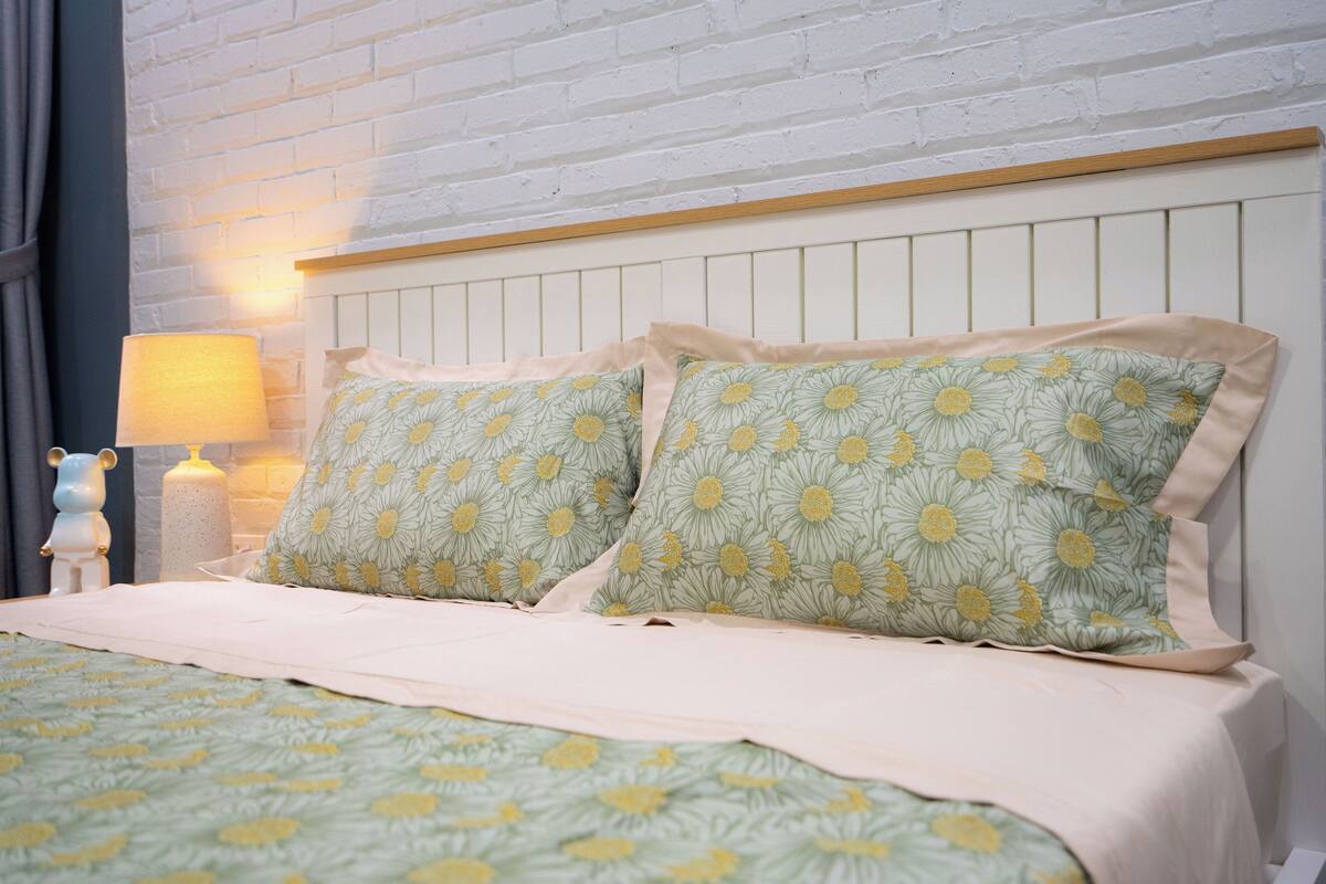 A neatly made bed with floral bedding and a headboard against a white brick wall.