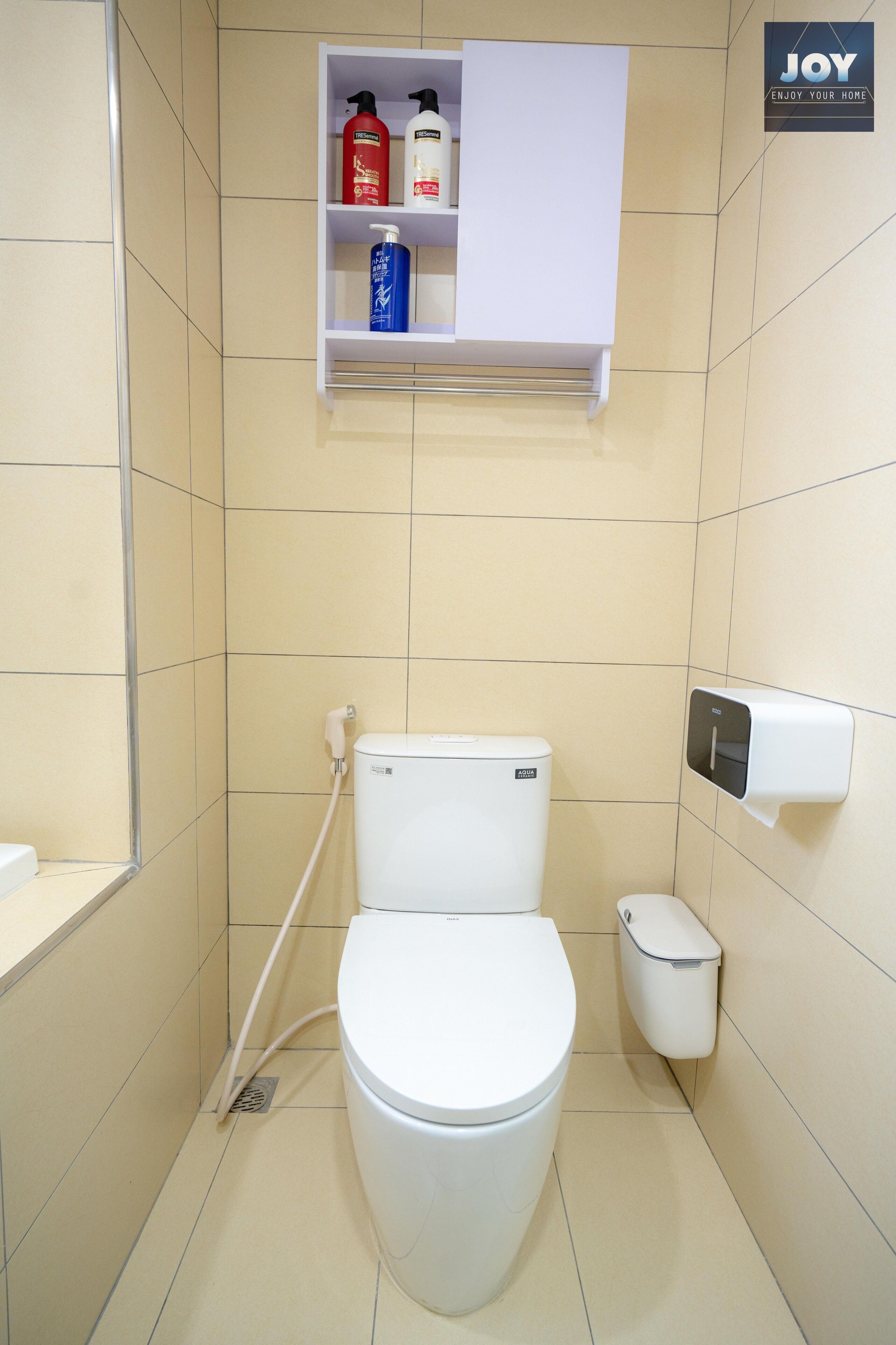 A small, modern bathroom with a toilet, a shelf with toiletries, and a soap dispenser.