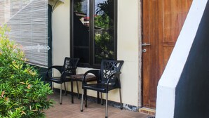 A patio with two black chairs and a table, a wooden door with the number 3, and a window with a view of greenery. - Hotel O We Bro Kost (Nginamanu)