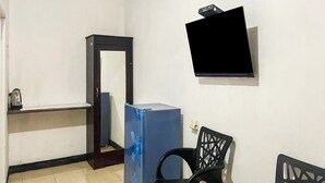 A small room with a blue refrigerator, a wooden cabinet, a black chair, and a wall-mounted TV. - Hotel O We Bro Kost (Nginamanu)