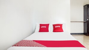 A bed with white bedding and two red pillows with "OYO" branding, a red patterned throw, and a dark wooden wardrobe against a white wall. - Hotel O We Bro Kost (Nginamanu)
