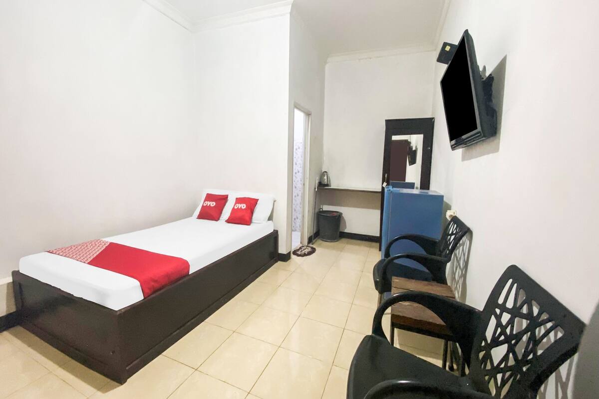 A single bed with a red and white bedspread, a small bedside table, and a chair.