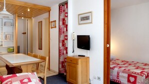 A small, cozy room with a wooden ceiling, a bed with a red and white quilt, a desk with a television, and a chair. - Comfortable Apartment in Tignes, Pet Friendly (Tignes)