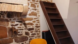 A room with a stone wall, a wooden sculpture, and a wooden ladder. - Charming 2-Person Cottage with Garden & Shared Amenities in Montenay (Montenay)