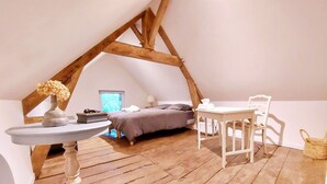 A cozy attic bedroom with a sloped ceiling, a bed, a small table, and a chair. - Charming 2-Person Cottage with Garden & Shared Amenities in Montenay (Montenay)
