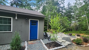 A house with a blue door, a small garden with a tree, and a patio area with outdoor furniture. - Newly renovated waterfront cottage with spectacular sunset views (Sullivan)