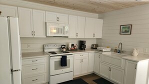 A kitchen with white cabinets, a stove, a microwave, a sink, and a coffee maker. - Newly renovated waterfront cottage with spectacular sunset views (Sullivan)