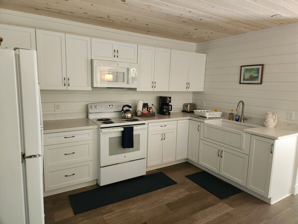 Una cocina con gabinetes blancos, estufa, microondas, lavaplatos y cafetera.
