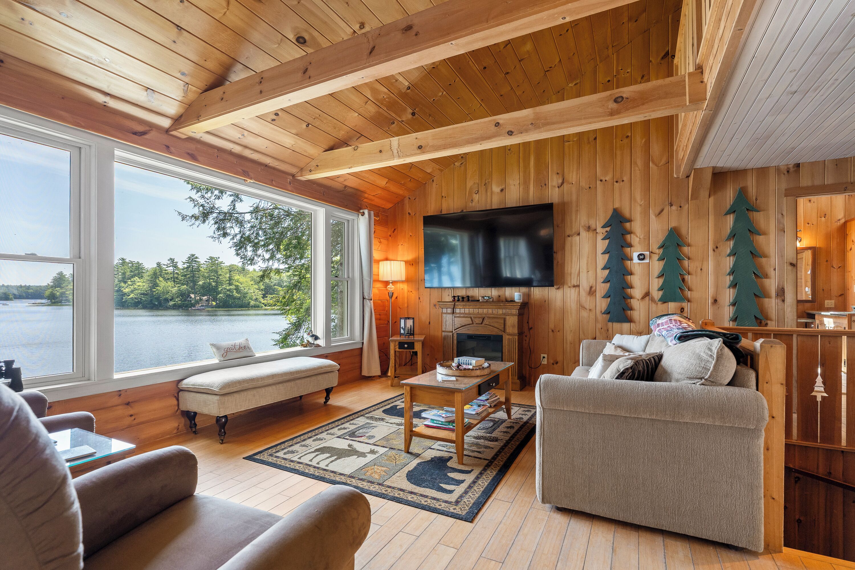 A cozy cabin-style room with a large window, a fireplace, a television, and a comfortable seating area.