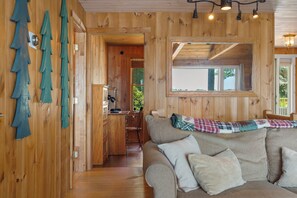 A wooden interior with a sofa, a mirror, and a view of the outdoors.