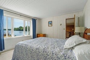 A bedroom with a bed, a window with curtains, a wooden dresser, and a door leading to another room.