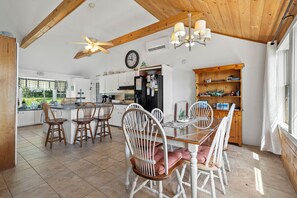 A spacious kitchen with a dining area, wooden ceiling beams, a ceiling fan, and a large window providing natural light.
