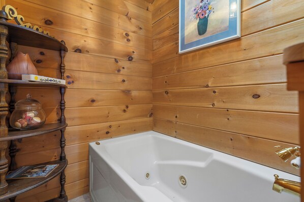 A wooden-paneled bathroom with a white bathtub, shelves with decorative items, and a framed picture on the wall.