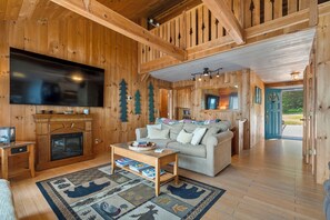 A cozy cabin interior with a fireplace, a large flat-screen TV, a sofa, and a coffee table.