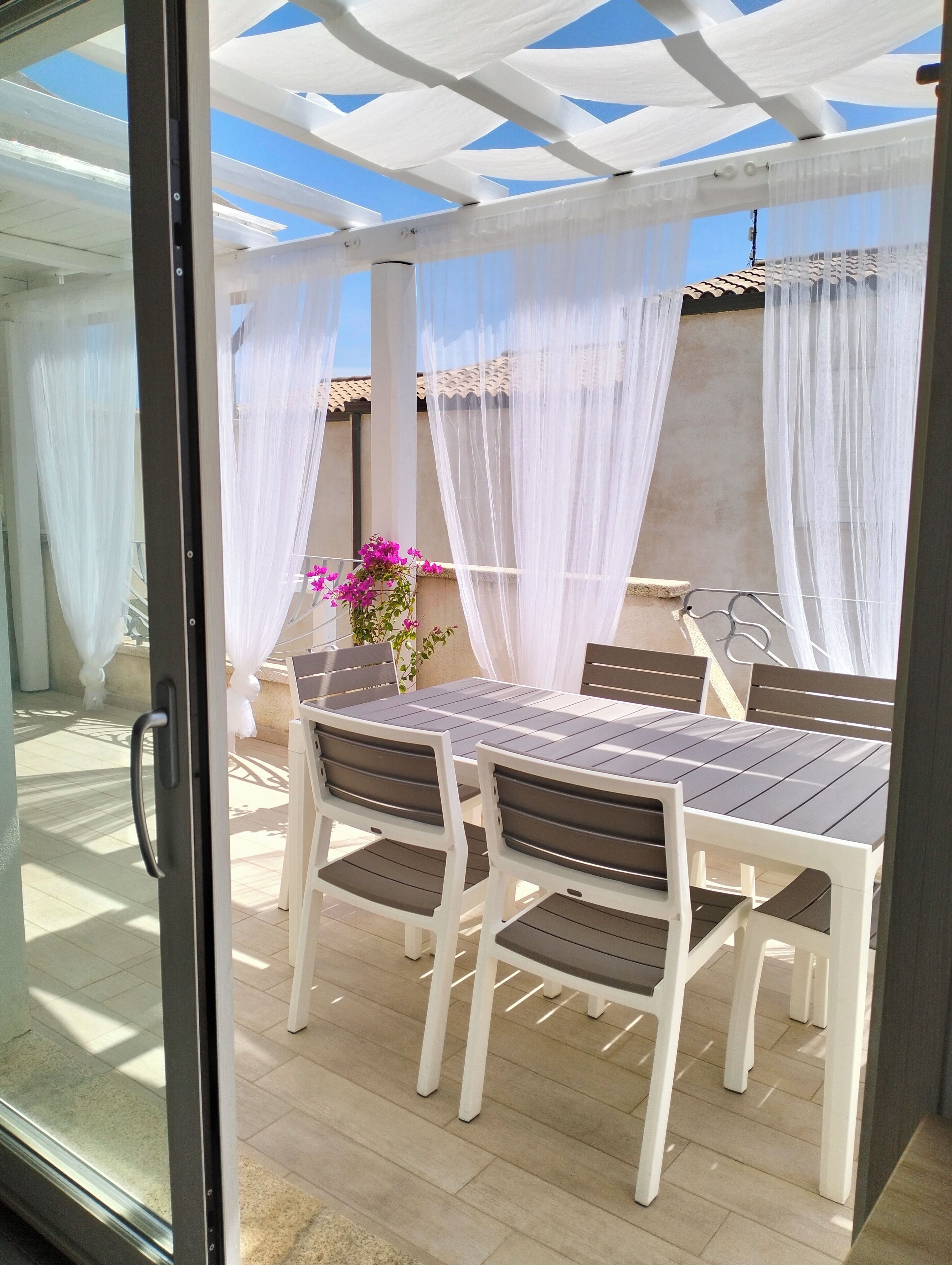 Patio esterno con tavolo e sedie, coperto da un tendone bianco.
