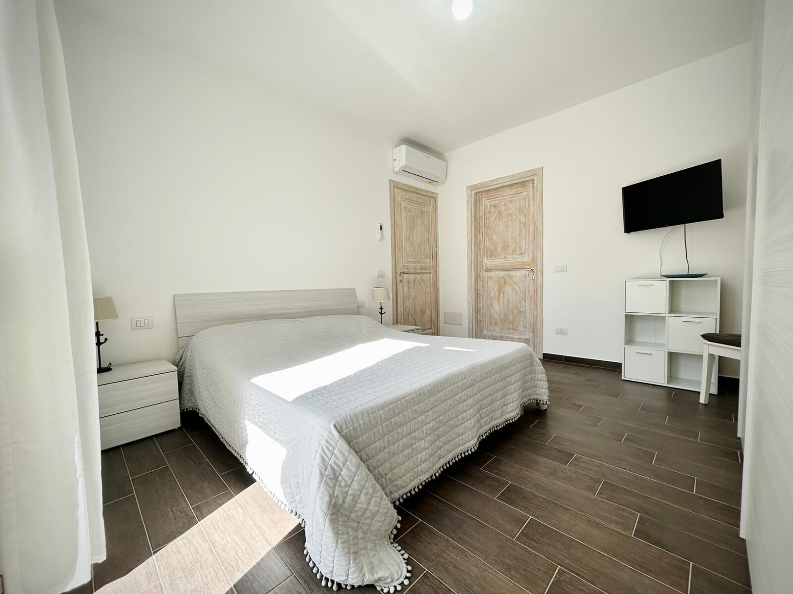 Une chambre à coucher avec un lit, des tables de chevet, une télévision et une armoire.