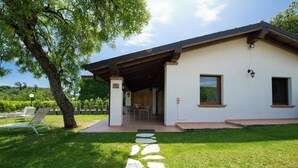 A modern house with a covered patio, stone pathway, and a lawn with outdoor furniture. - Il Podere del Bardo (Puegnago del Garda)