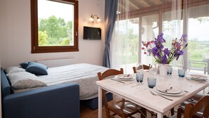 A room with a bed, a dining table set for two, and a large window with curtains. - Il Podere del Bardo (Puegnago del Garda)