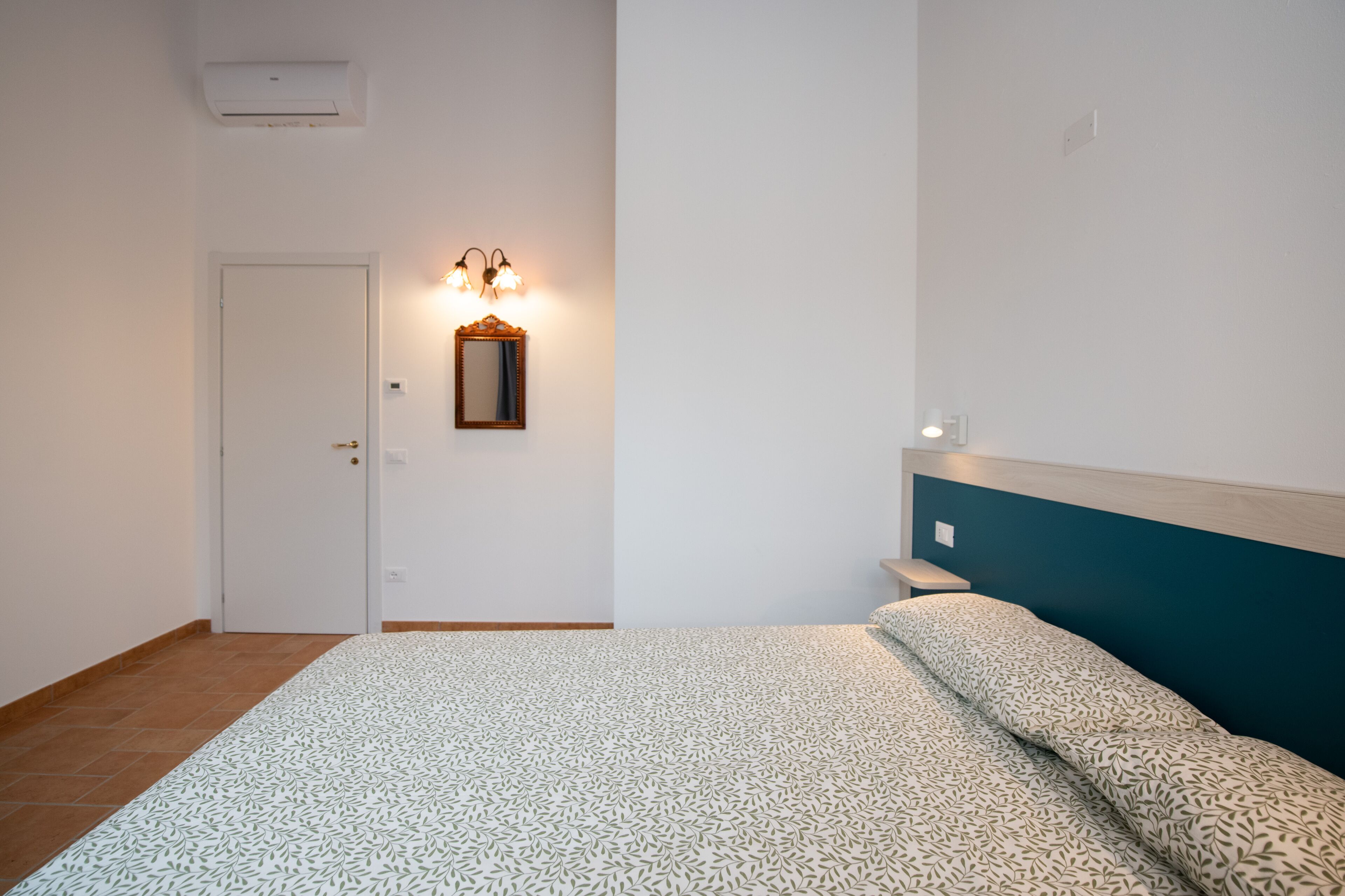 A bedroom with a bed, a wall-mounted mirror, and a light fixture.