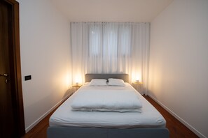 Un lit bien fait, avec du linge de lit blanc, deux lampes de chevet et des rideaux légers.
