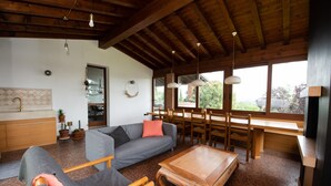 Amplia sala de estar con techo de madera, un sofá gris, una mesa de centro de madera y una mesa de comedor con sillas.
