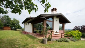 Una casa moderna con un amplio ventanal de vidrio, una terraza de madera y una jardinera de piedra.