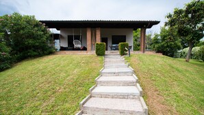 Una casa con porche cubierto, una escalera de hormigón que conduce a la entrada y un pequeño jardín.