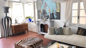 Un salon avec un canapé, un pouf, une cheminée et des œuvres d’art accrochées au mur.