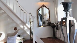 Un escalier avec des rampes blanches, un lustre, un miroir et une table sur laquelle est posé un vase.