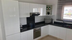 Una cocina moderna con armarios blancos, una encimera negra, horno empotrado y una ventana con persianas.