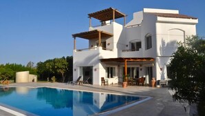 Una casa moderna de dos pisos con piscina, mobiliario exterior y una pérgola.