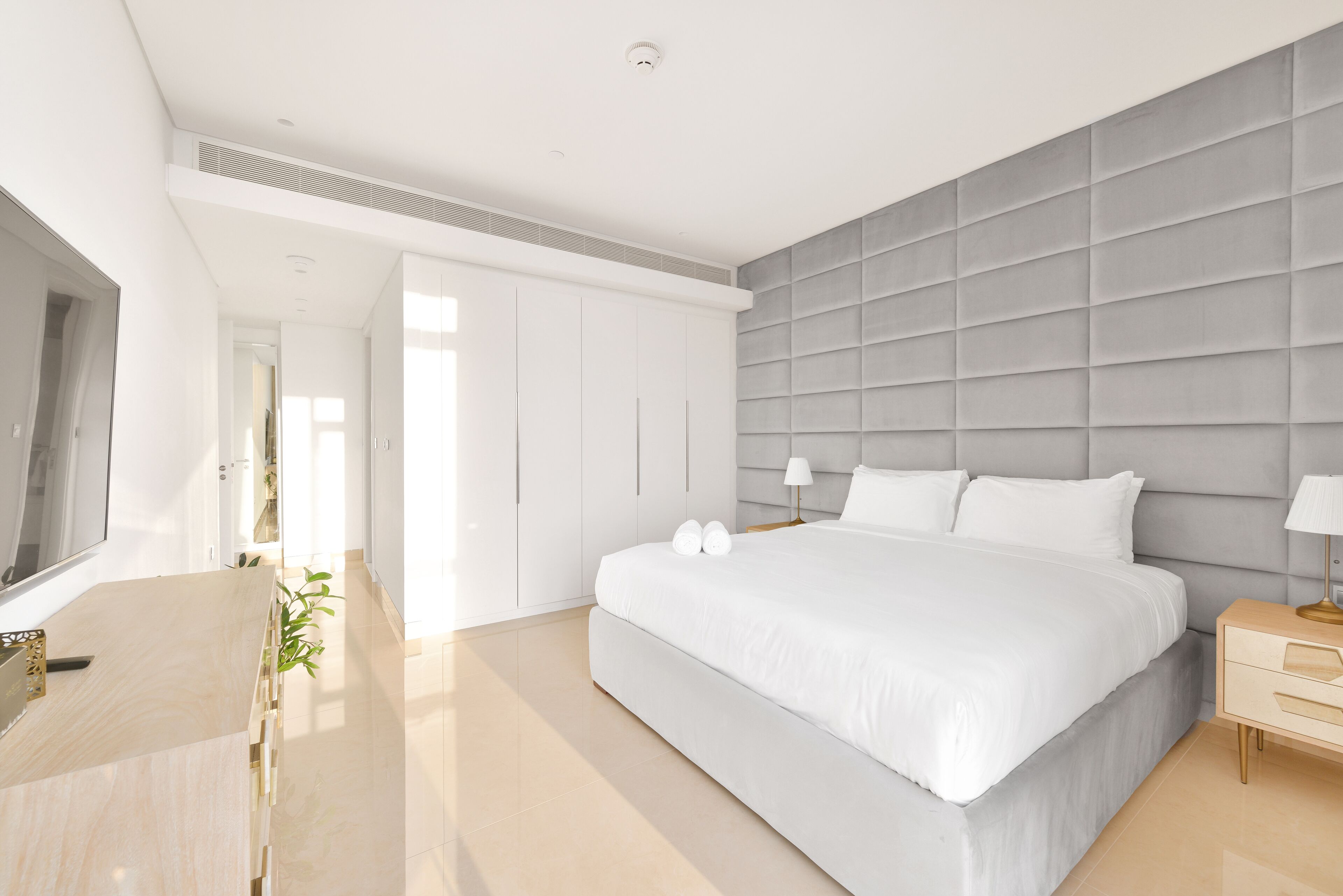 A modern bedroom with a large bed, a flat-screen TV, a bedside table, and a wardrobe.