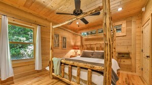 A wooden cabin bedroom with a four-poster bed, a ceiling fan, and a window with curtains. -  Log cabin between Boone and Banner Elk-hot tub-game room-fire pit-private-cozy (Banner Elk)