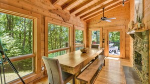 A wooden cabin interior with large windows, a dining table, benches, a fireplace, and a ceiling fan. -  Log cabin between Boone and Banner Elk-hot tub-game room-fire pit-private-cozy (Banner Elk)