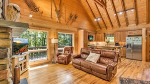 A spacious cabin interior with a wooden ceiling, a fireplace, a leather sofa, and a kitchen area. -  Log cabin between Boone and Banner Elk-hot tub-game room-fire pit-private-cozy (Banner Elk)