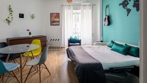 A modern bedroom with a bed, a desk with chairs, a world map on the wall, and a guitar. - PennyLane Apartment 1 (Roma)