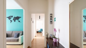 A hallway with a world map on the walls, a sofa, a small table with a plant, and a door leading to another room. - PennyLane Apartment 1 (Roma)