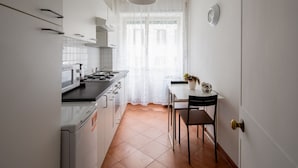 A compact kitchen with a stove, sink, and a dining area with a table and chairs. - PennyLane Apartment 1 (Roma)