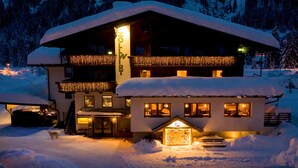 A snow-covered lodge with a balcony adorned with lights, a lit entrance, and a visible restaurant area. - Zollwirt (Sankt Jakob in Defereggen)