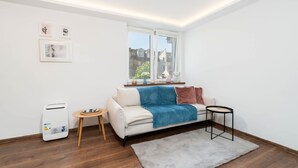 Un salon moderne avec un canapé blanc, un plaid bleu, une petite table ronde et un radiateur portatif.