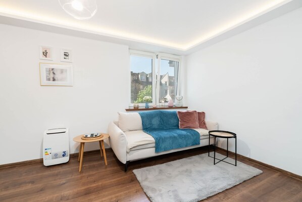 A modern living room with a white sofa, a blue throw blanket, a small round table, and a standing heater.