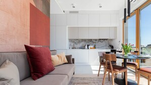 A modern living room with a sofa, a dining table, and chairs. A kitchen is visible in the background with white cabinets and a marble backsplash. - Stylish Apartment with Balcony | Parking | View of the Motława River (Gdansk)