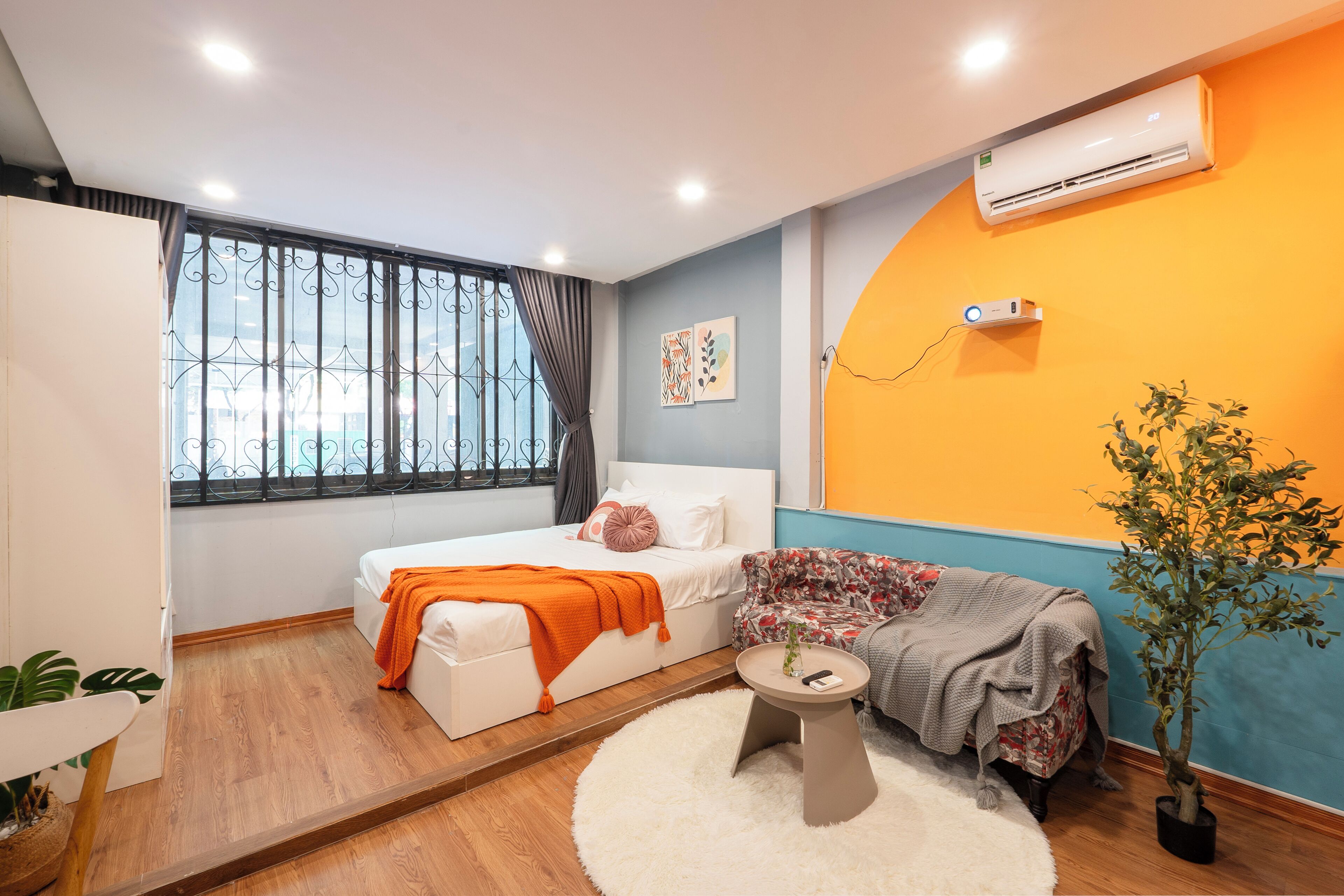 A compact bedroom with a bed, a sofa, a small table, and a potted plant.