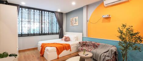A compact bedroom with a bed, a sofa, a small table, and a potted plant.