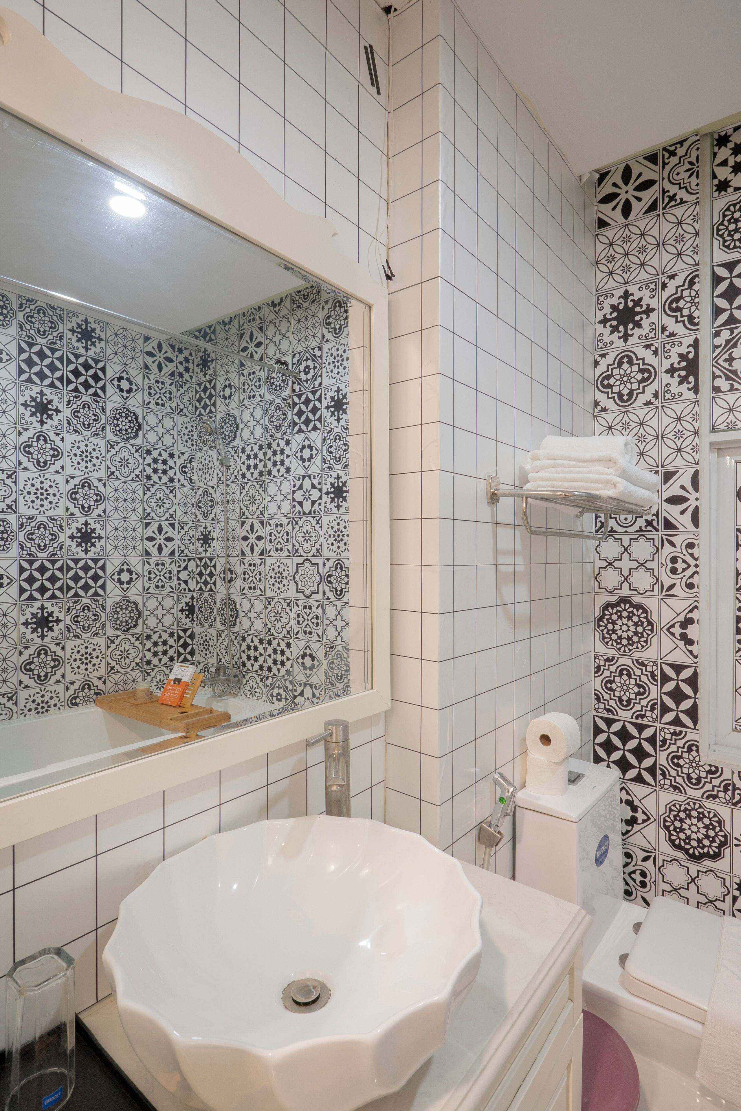 A bathroom with a white sink, a mirror, a toilet, and patterned tiles on the walls.