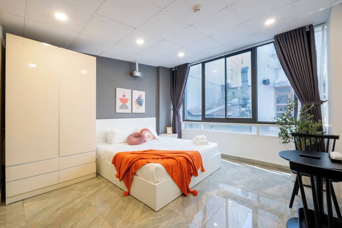 A modern hotel room with a large bed, a small table, and a view of the city through the window.