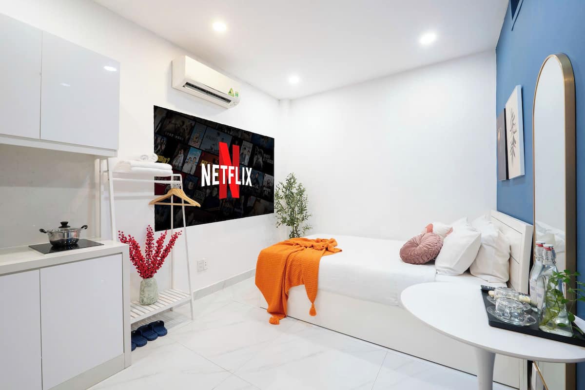 A modern hotel room with a white sofa, a small table with a tray, a TV wall-mounted above the sofa, and a white wardrobe.