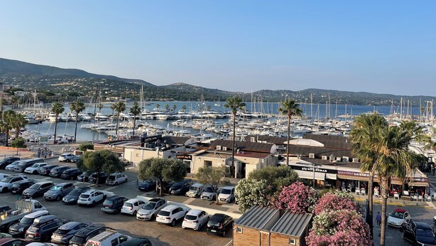 A marina with numerous boats, a parking lot with cars, and a view of the coastline with hills in the background. - Penthouse near Saint Tropez Cavalaire sur mer Port view, Beach... (Cavalaire-sur-Mer)